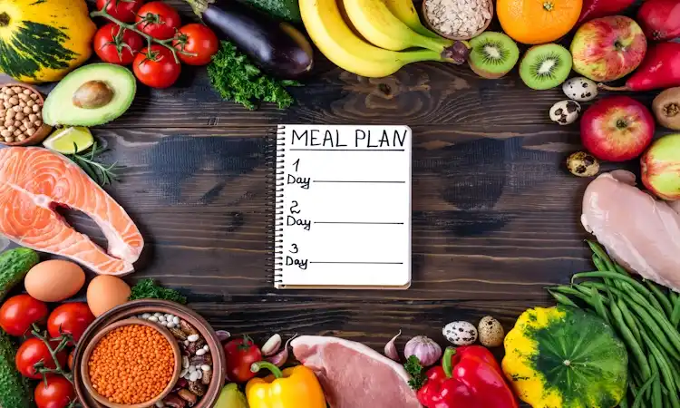 Metabolic Flexibility Meal Plan (Carb Days) A notebook labeled "Meal Plan" is centered on a wooden table, surrounded by colorful fruits, vegetables, salmon, chicken, and eggs, evoking health and balance.